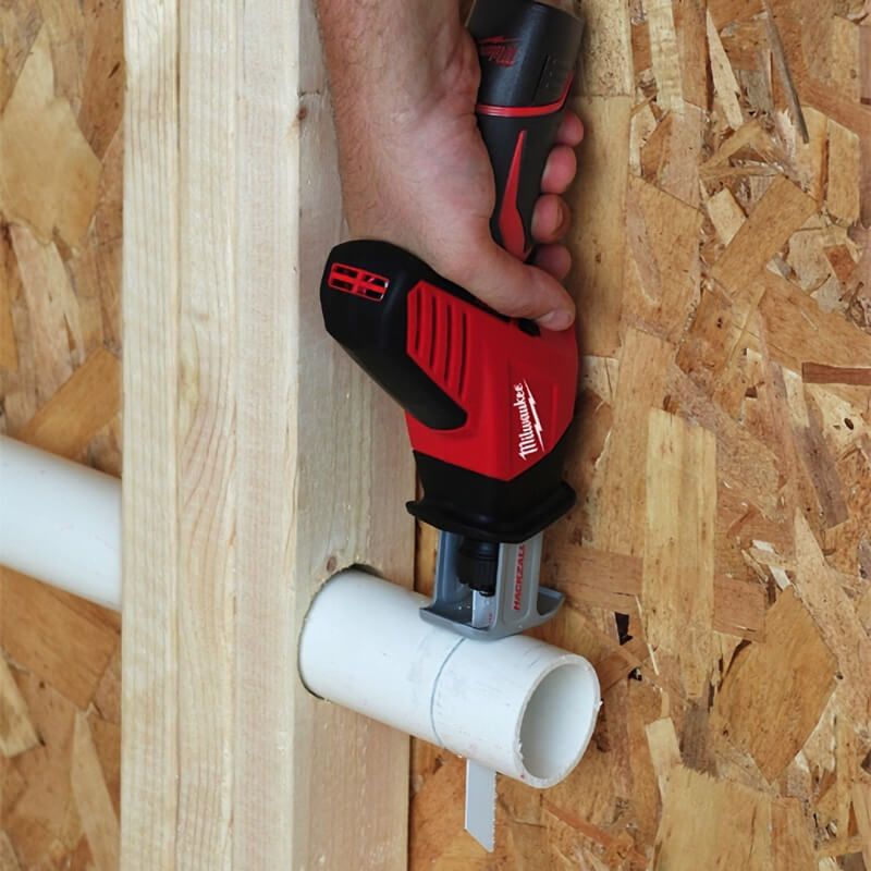 Hand using a Milwaukee Hackzall saw with a blade cutting a white PVC pipe mounted on wood.