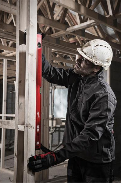 Man wearing a white hard hat using a red Milwaukee Level Slim 80cm to check vertical alignment on wooden framing.