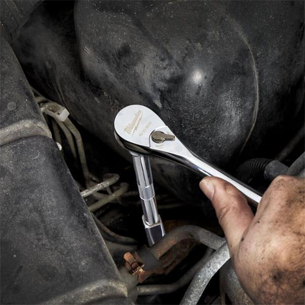 Milwaukee 1/4" driver ratchet with socket attached, used on a vehicle engine by a hand.