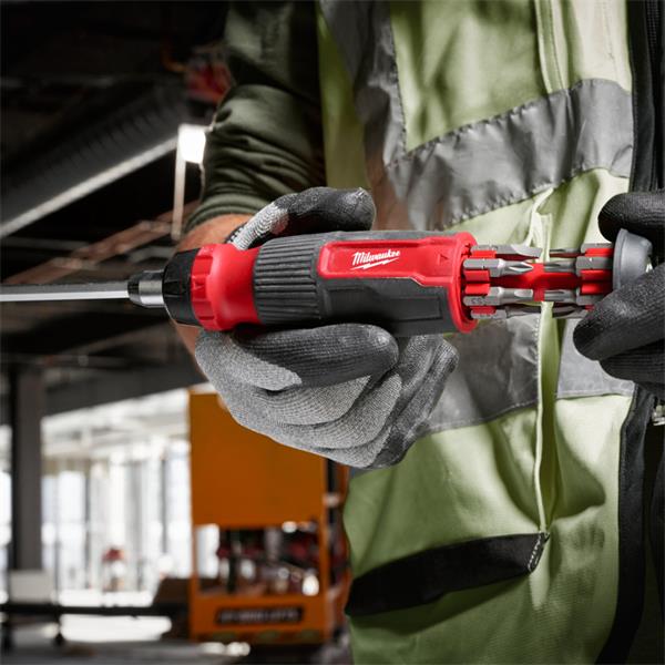 Hands wearing gloves hold a Milwaukee 14 in 1 Ratchet Multi-Bit Screwdriver with bits stored in the handle.