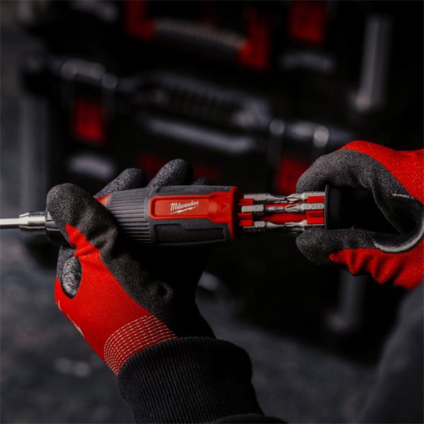 Hands wearing red and black gloves holding a Milwaukee 14 in 1 ratchet multi-bit screwdriver with bits extended.