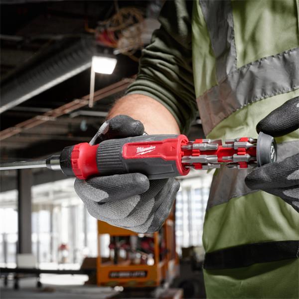 Milwaukee 27 in 1 Ratchet Multi-Bit Screwdriver held by a worker in a construction setting with bits extended.