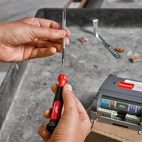 Hands holding a Milwaukee 4 in 1 Precision Multi-Bit Screwdriver with interchangeable bit above a workbench.