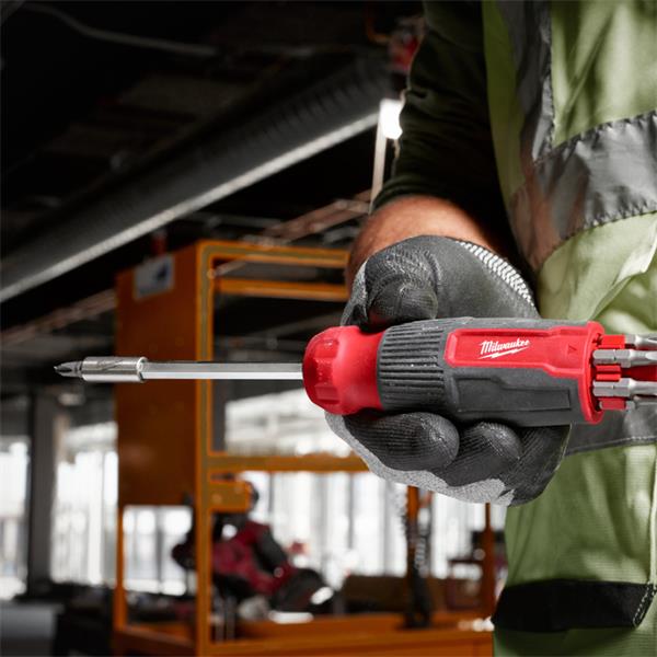 Hand holding Milwaukee 14 in 1 Multi-Bit Screwdriver with extended bit in a workshop setting.