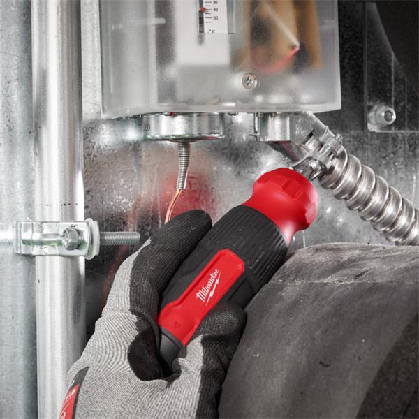 Hand in glove holding Milwaukee 14 in 1 Multi-Bit Screwdriver tightening a metal fitting in an industrial setting.