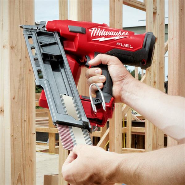 Hand holding Milwaukee M18 FUEL cordless framing nailer loading nails at a wooden construction site