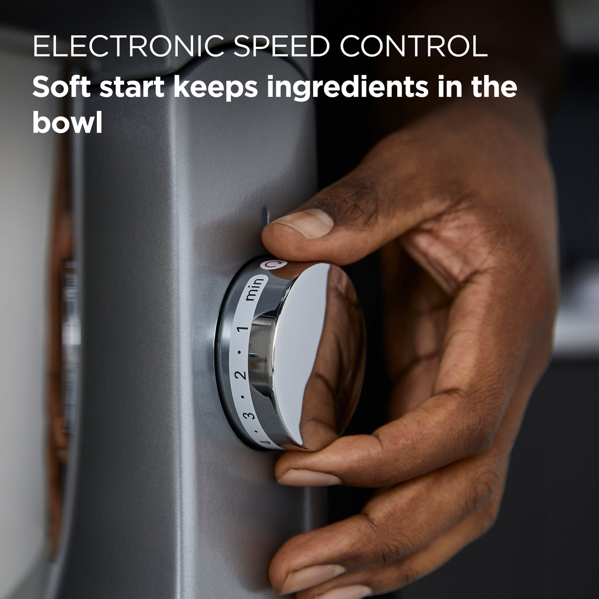 Close-up of a hand adjusting the speed control dial on a silver kitchen mixer machine.