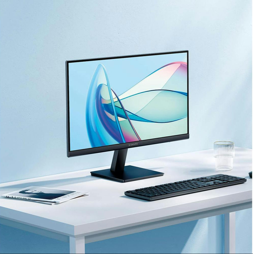 Xiaomi 21.45'' A22i FHD monitor on a white desk with a keyboard, magazine, and glass cup nearby.