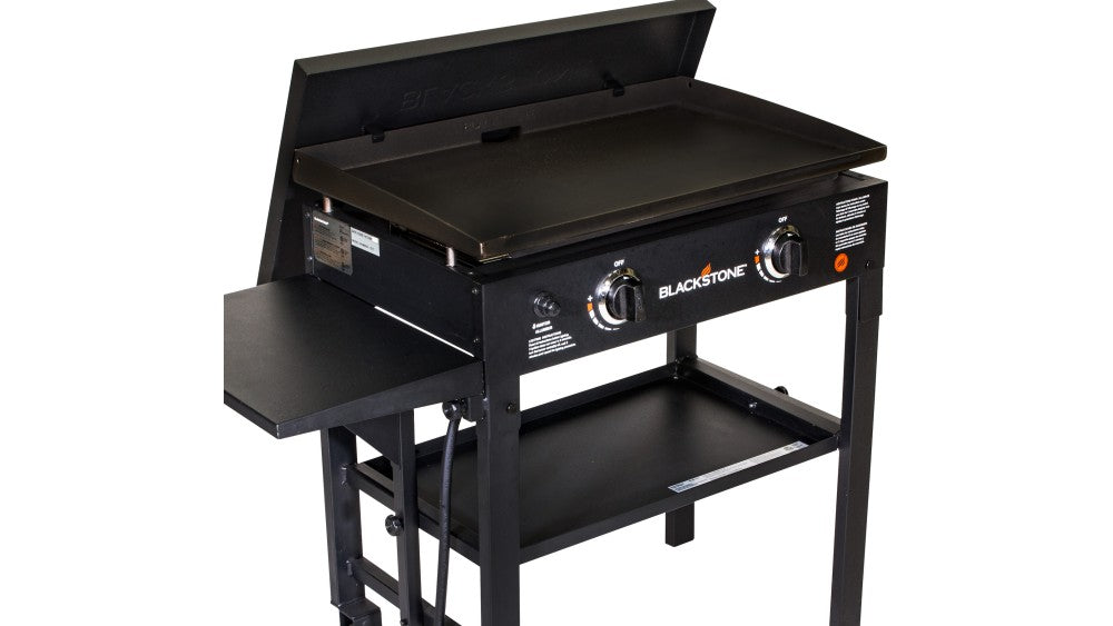 Blackstone 28'' griddle with open hard cover, two control knobs, side shelf, and lower storage shelf.