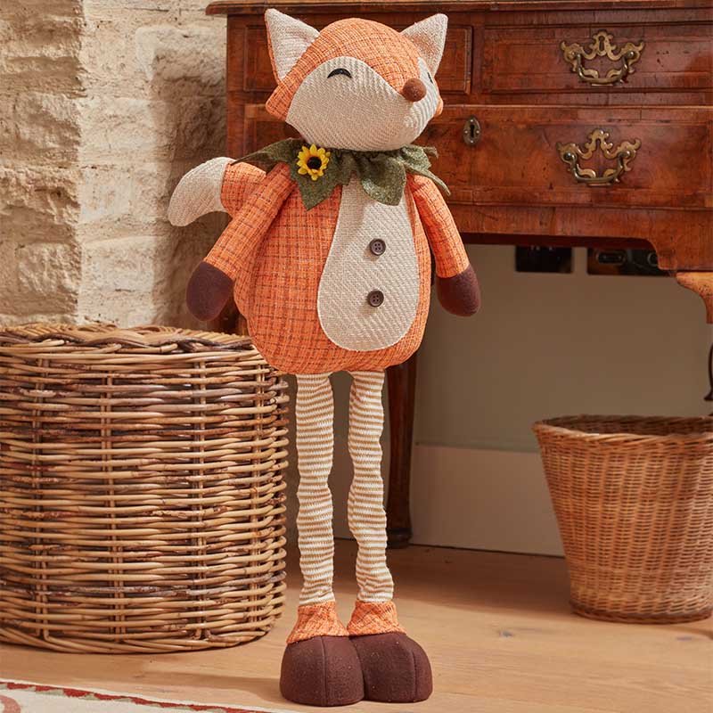 Large handcrafted plush Mr Fox decoration with long striped legs, orange body, and sunflower collar standing indoors by