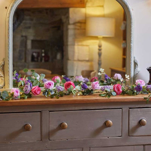 Eden Blooms Garland 180cm with pink and purple flowers and green leaves displayed on a wooden dresser.