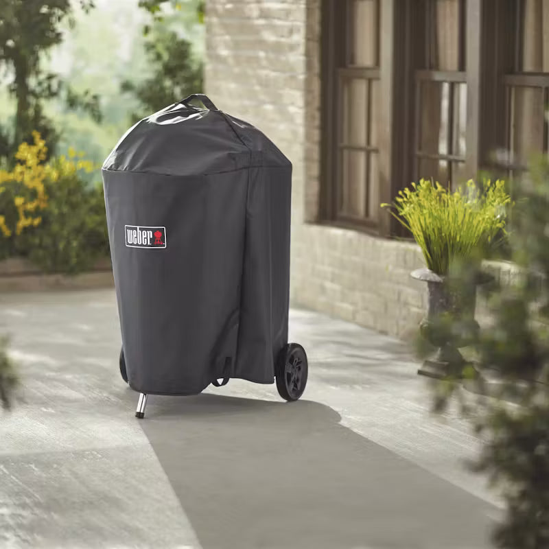 Weber Premium Barbecue 57cm Master Touch covered with a black protective cover outdoors on a patio