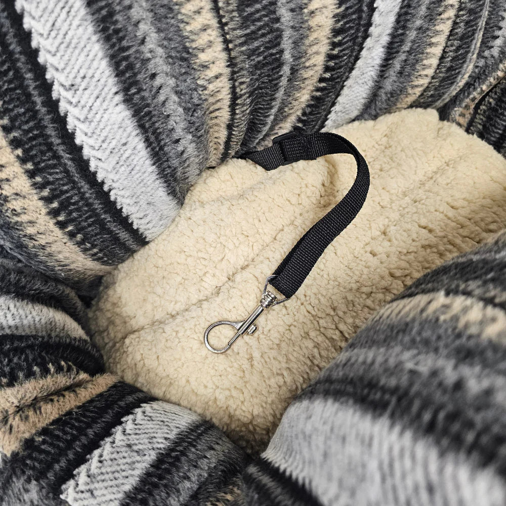 Close-up of a soft, striped dog car seat with a beige fleece interior and attached black safety leash clip.