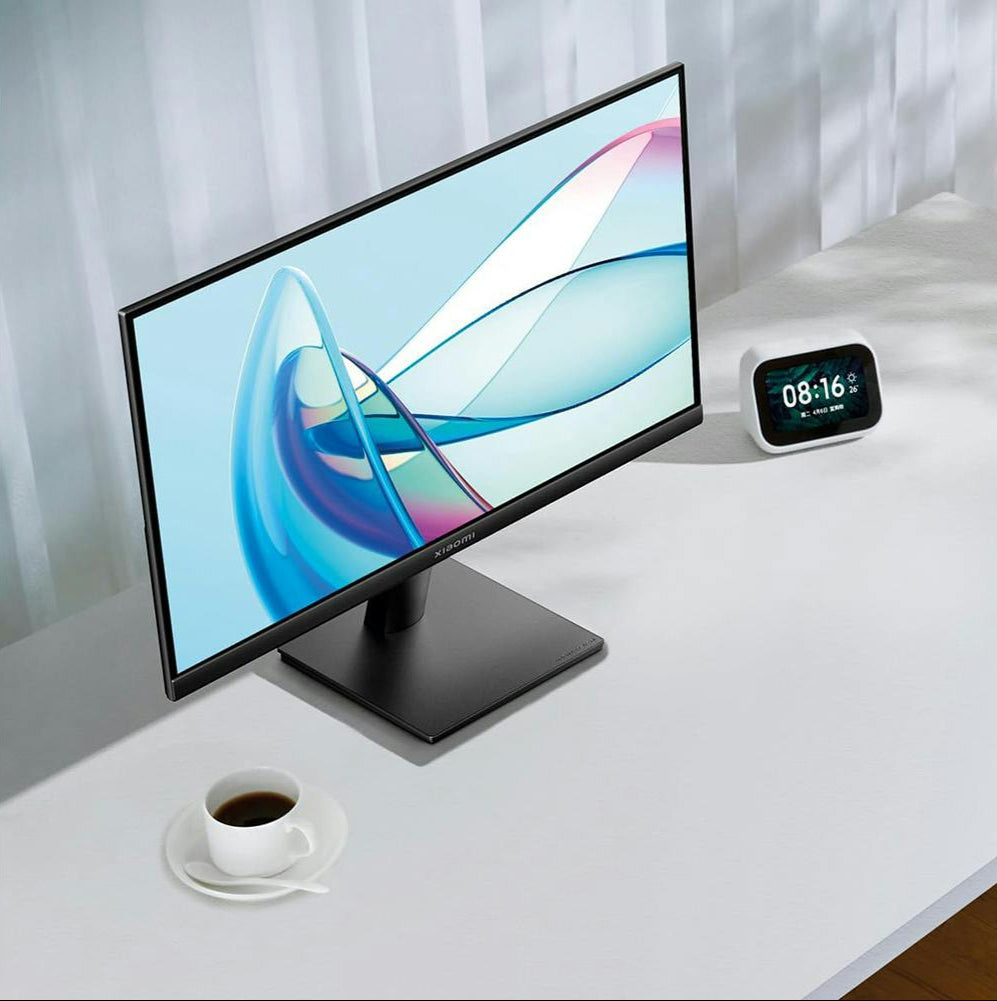 Xiaomi 21.45'' A22i FHD monitor on a white desk with a cup of coffee and a digital clock nearby.