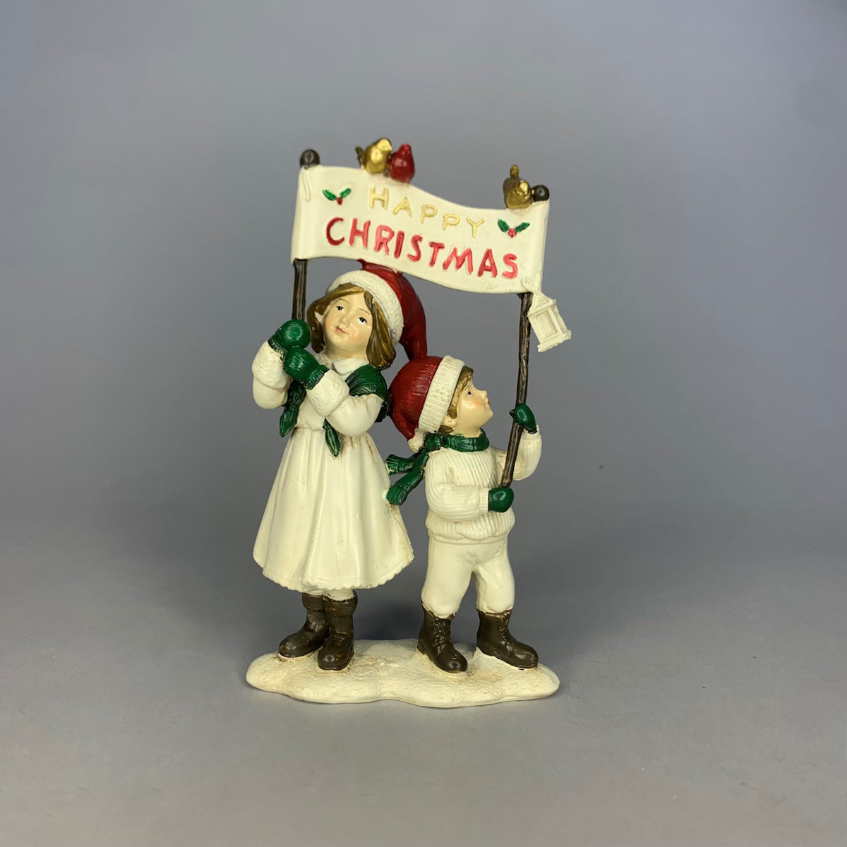 Children figurine ornament holding a "Happy Christmas" sign, dressed in winter clothes, 13 cm tall.