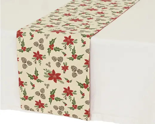 A festive table runner with a cream background printed with red poinsettias, green holly leaves, pinecones, and red berries, draped over a white table.