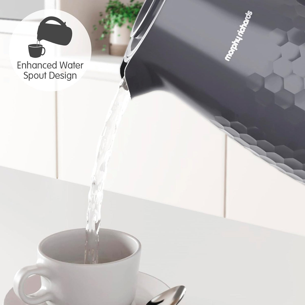 Grey Morphy Richards Hive Kettle pouring water into a white cup with saucer and spoon on a white surface