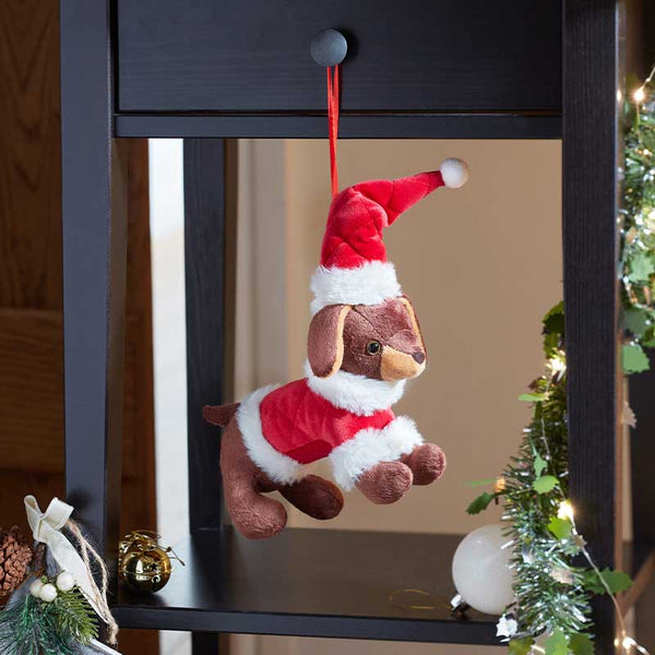 A plush puppy Christmas ornament wearing a red Santa hat and red sweater with white trim