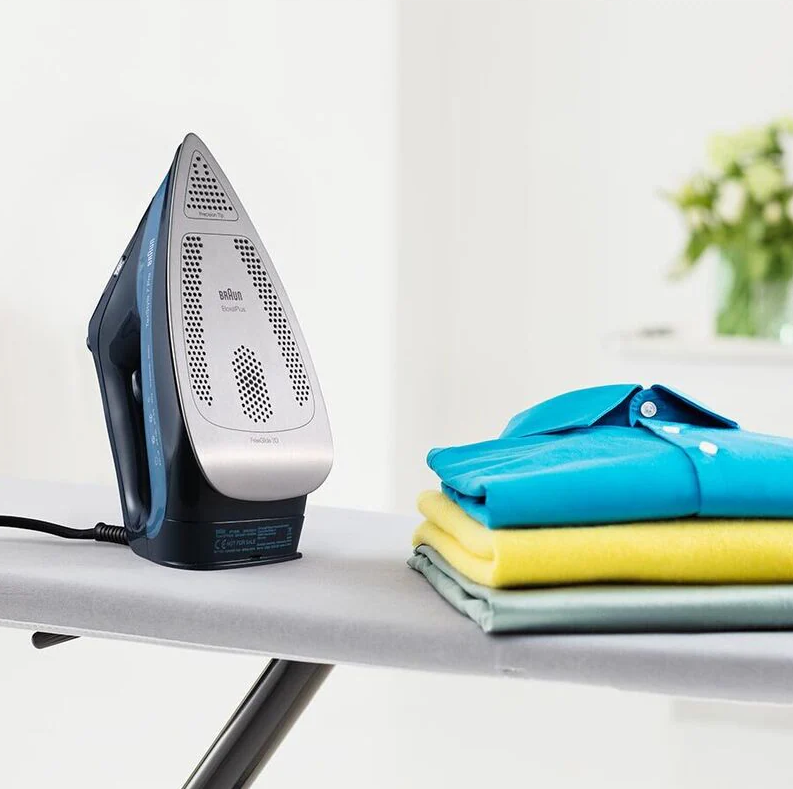 Braun Steam Generator Iron SI7160BL standing upright on ironing board next to folded colorful clothes