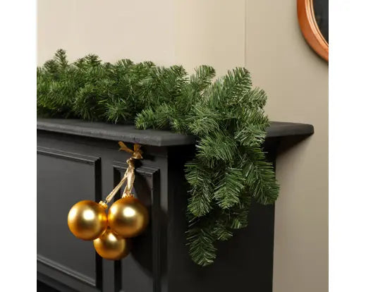 Imperial Garland draped over a black mantelpiece with three gold baubles hanging on the side.