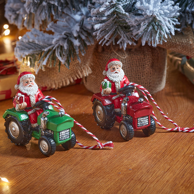 Two Christmas ornament figurines of Santa Claus driving tractor-shaped cars, one green and one red, with red-and-white striped tow ropes