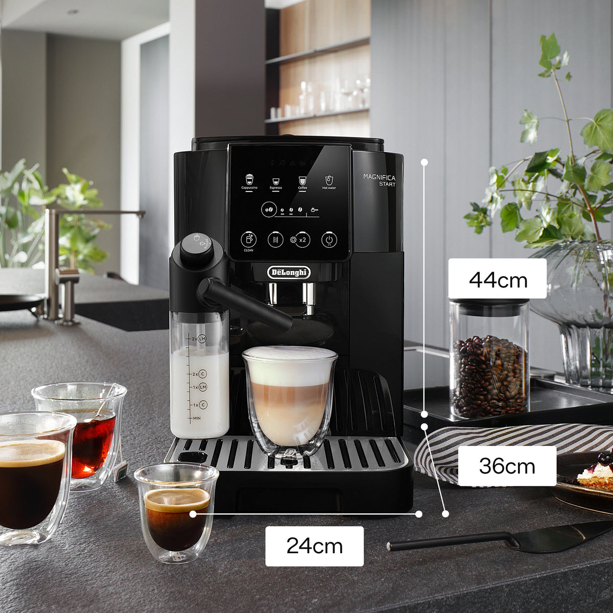 DeLonghi Magnifica Start coffee machine with milk frother, layered latte, espresso shots, and coffee beans jar nearby.