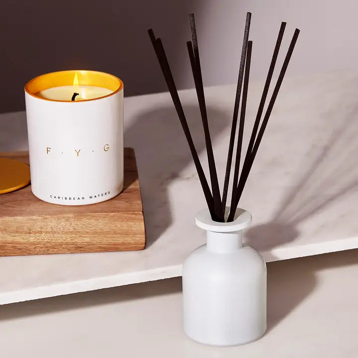 A Day At the Spa Diffuser F.Y.G with black reeds next to a lit candle on a wooden tray.