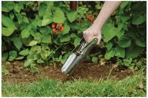 Kent & Stowe hand bulb planter digging into soil with a hand gripping the green handle outdoors.
