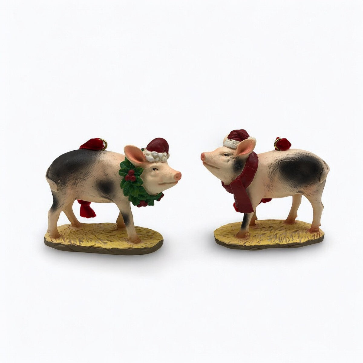 Two resin farm pig Christmas ornaments, one with a wreath and Santa hat, the other with a scarf and Santa hat.