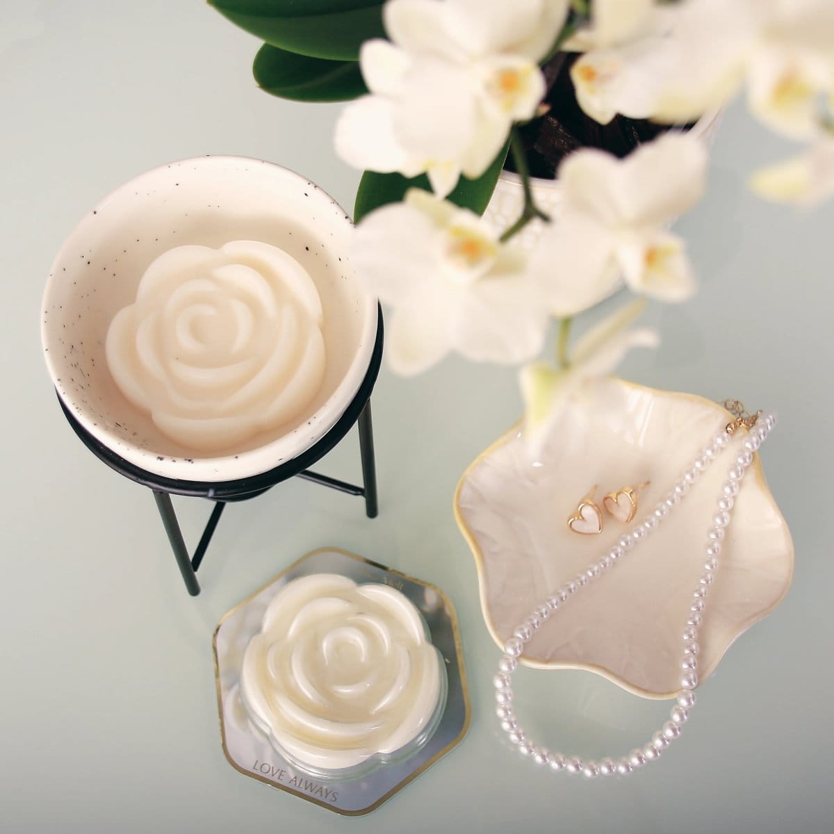 Fragrance wax melt Love Always shaped like a rose, shown with a ceramic wax warmer and jewelry dish with pearls and earrings.