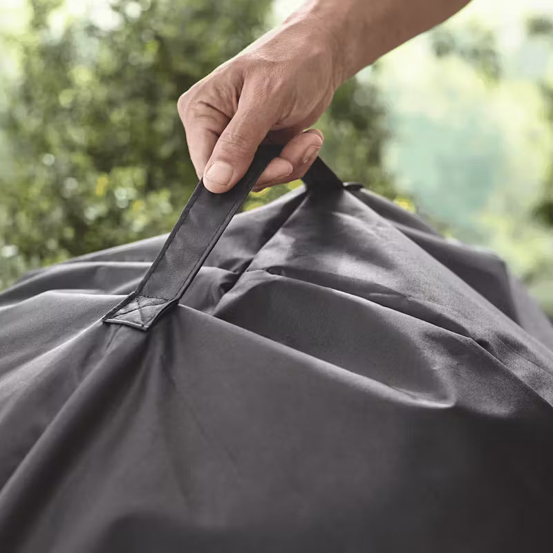 Hand lifting the black Weber Premium Barbecue 57cm Master Touch cover by its stitched handle outdoors.