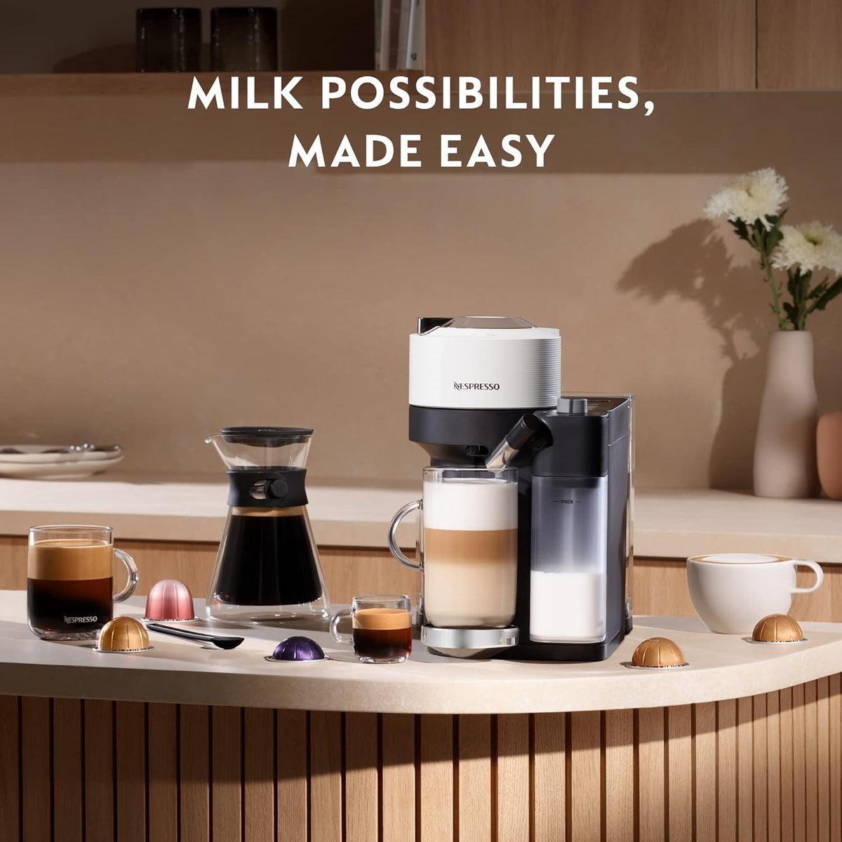 Delonghi Nespresso Vertuo Lattissima in white with milk frother, coffee cups, capsules, and a carafe on a counter.