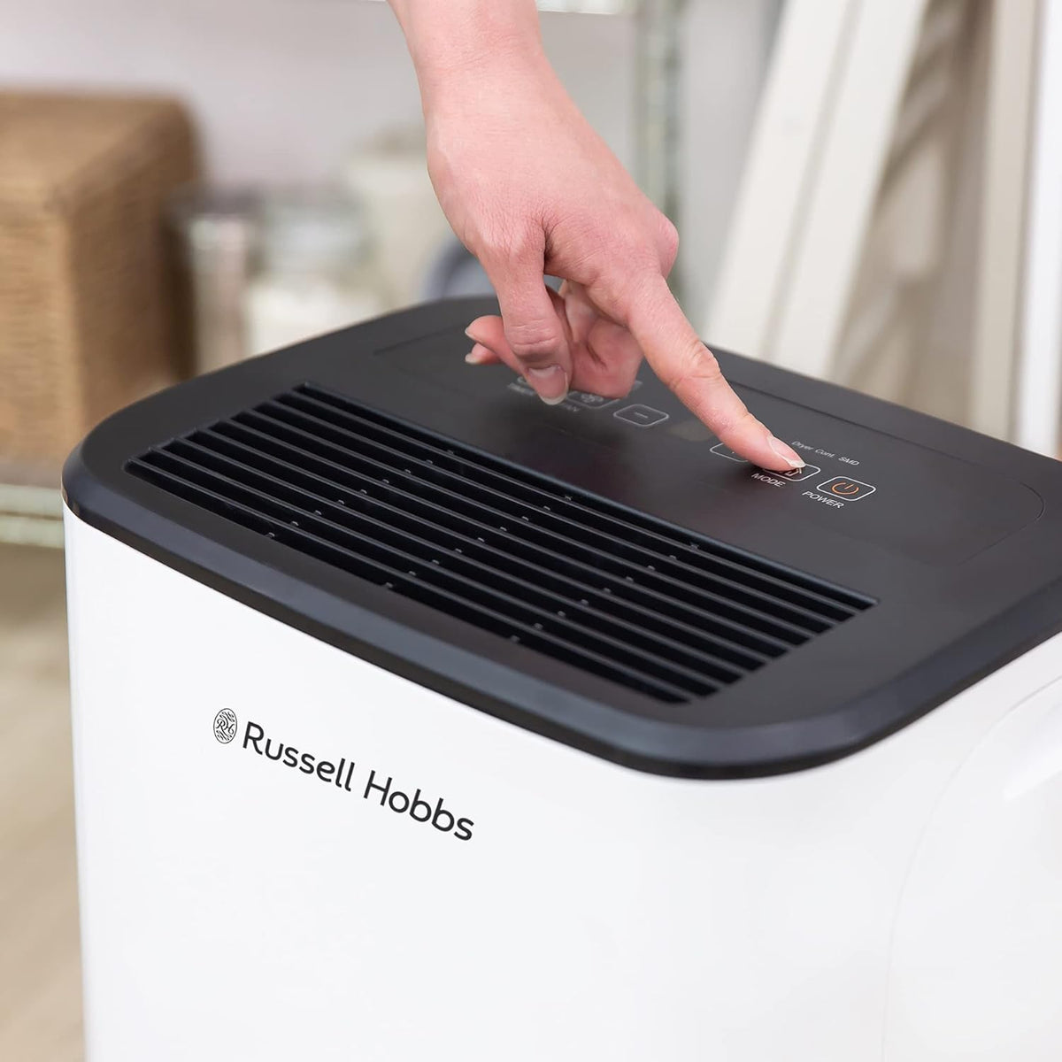 Hand pressing mode button on top control panel of Russell Hobbs 20L dehumidifier in white and black.