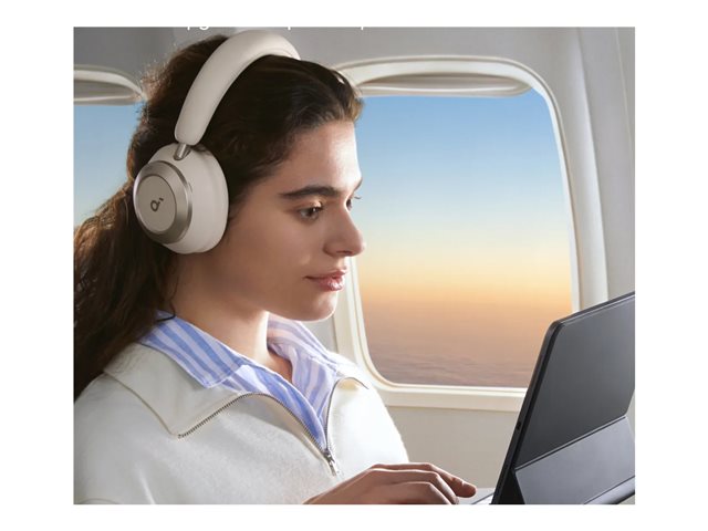Woman wearing white Soundcore Space One Pro headphones using a tablet on an airplane at sunset.