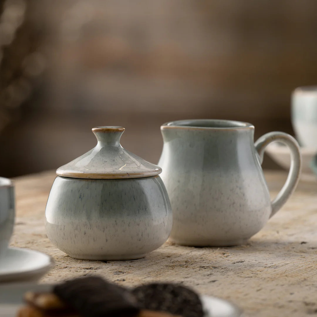Tivoli cream pitcher and covered sugar bowl in speckled cream ceramic on a wooden surface.