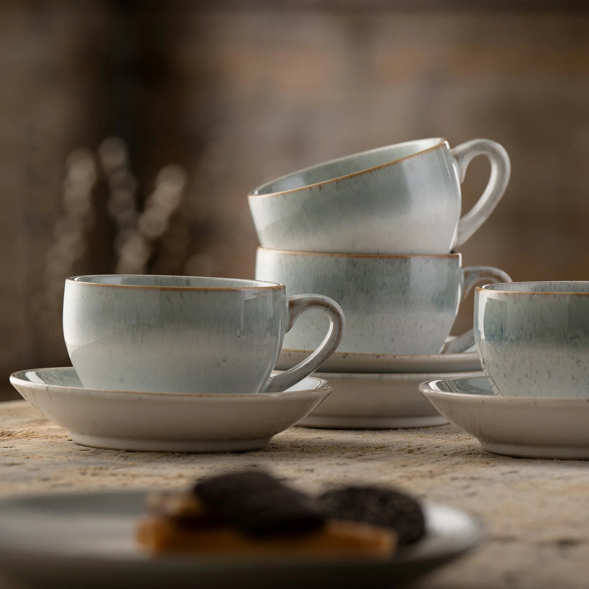 Stacked light blue-gray Tivoli cups with saucers on a rustic wooden surface, blurred background.