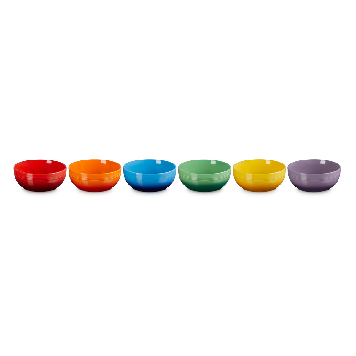 Six colorful Le Creuset Rainbow Coupe Cereal Bowls in red, orange, blue, green, yellow, and purple, side by side.