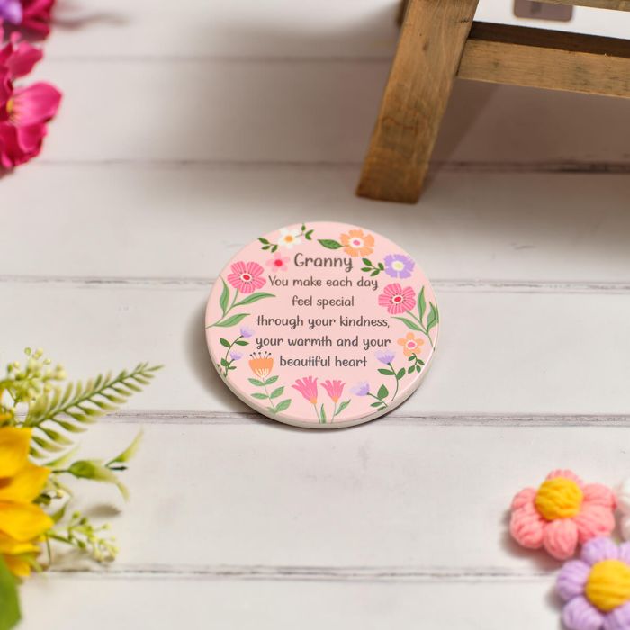 Round ceramic coaster with pink floral design and a heartfelt message for Granny on a white wooden surface.