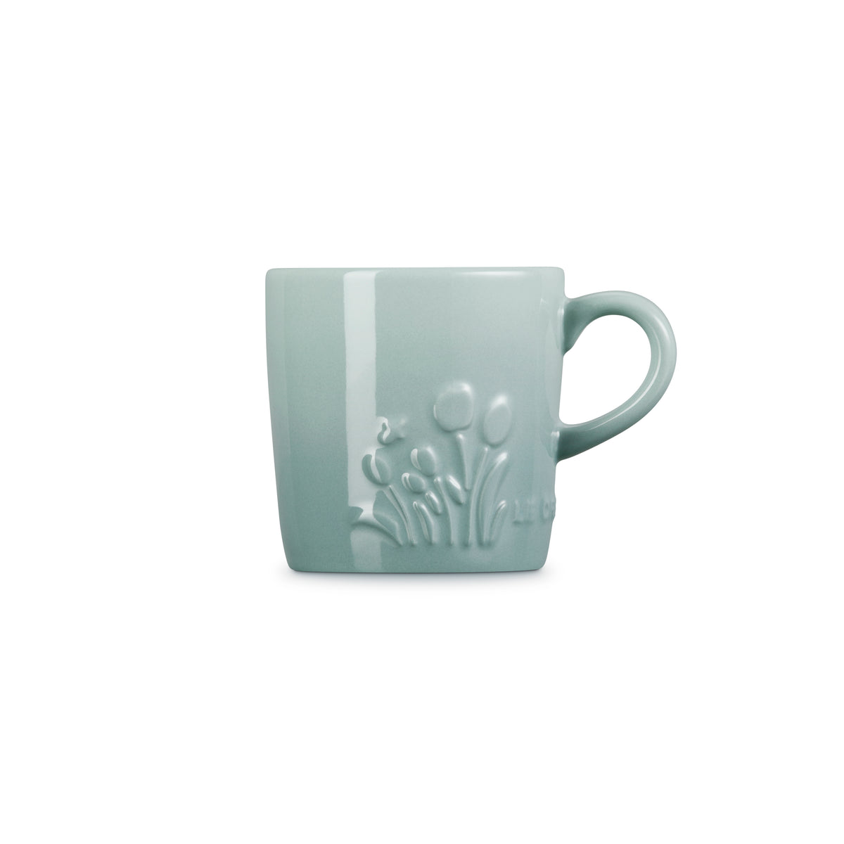 Le Creuset Capp Mug in sea salt color with embossed floral design, shown from the side with handle visible.