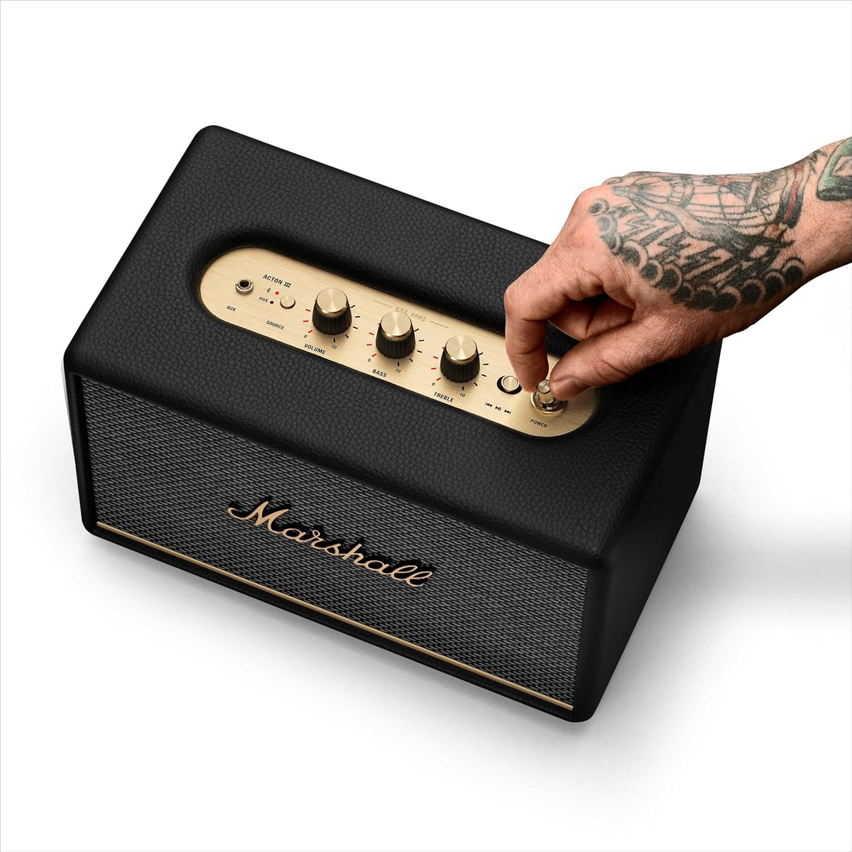 Marshall Acton III Bluetooth speaker in black with gold control knobs and a tattooed hand adjusting the power knob