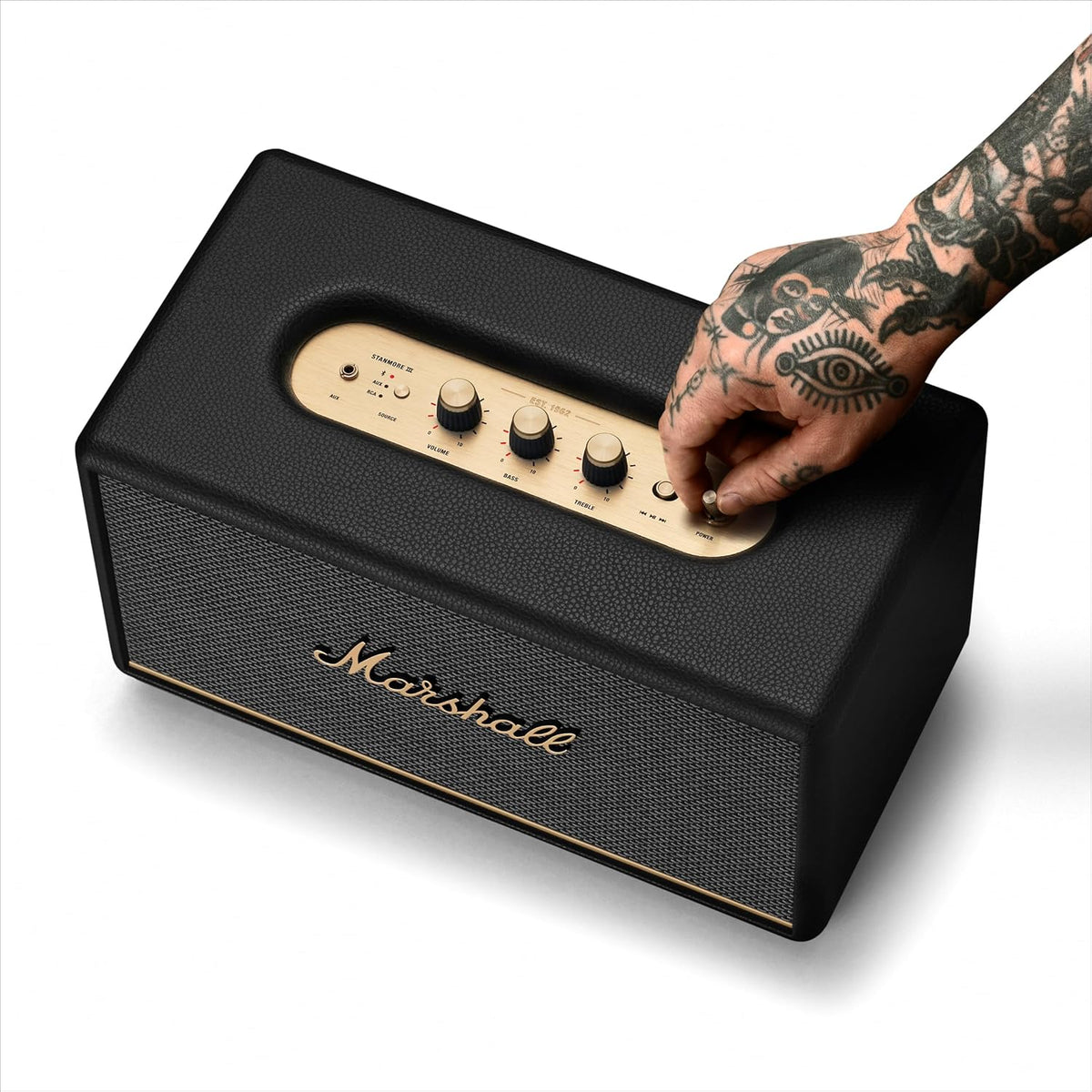 Marshall Stanmore III Bluetooth speaker in black with gold control panel and tattooed hand adjusting power knob.