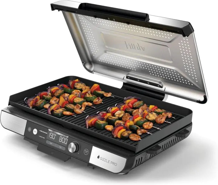 Ninja Sizzle Pro XL Grill with open lid, grilling skewers of shrimp and vegetables on the ribbed surface.