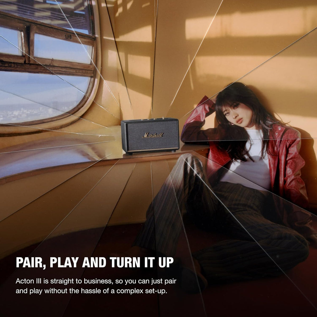 Marshall Acton III Bluetooth speaker in black on a curved wooden surface by a window with a woman sitting nearby