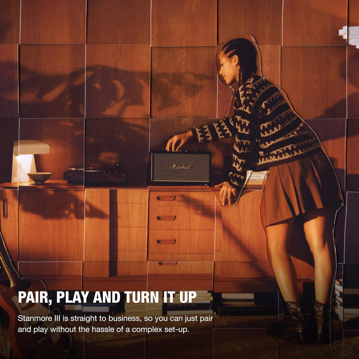 Woman adjusting black Marshall Stanmore III Bluetooth speaker on wooden cabinet in warm room lighting