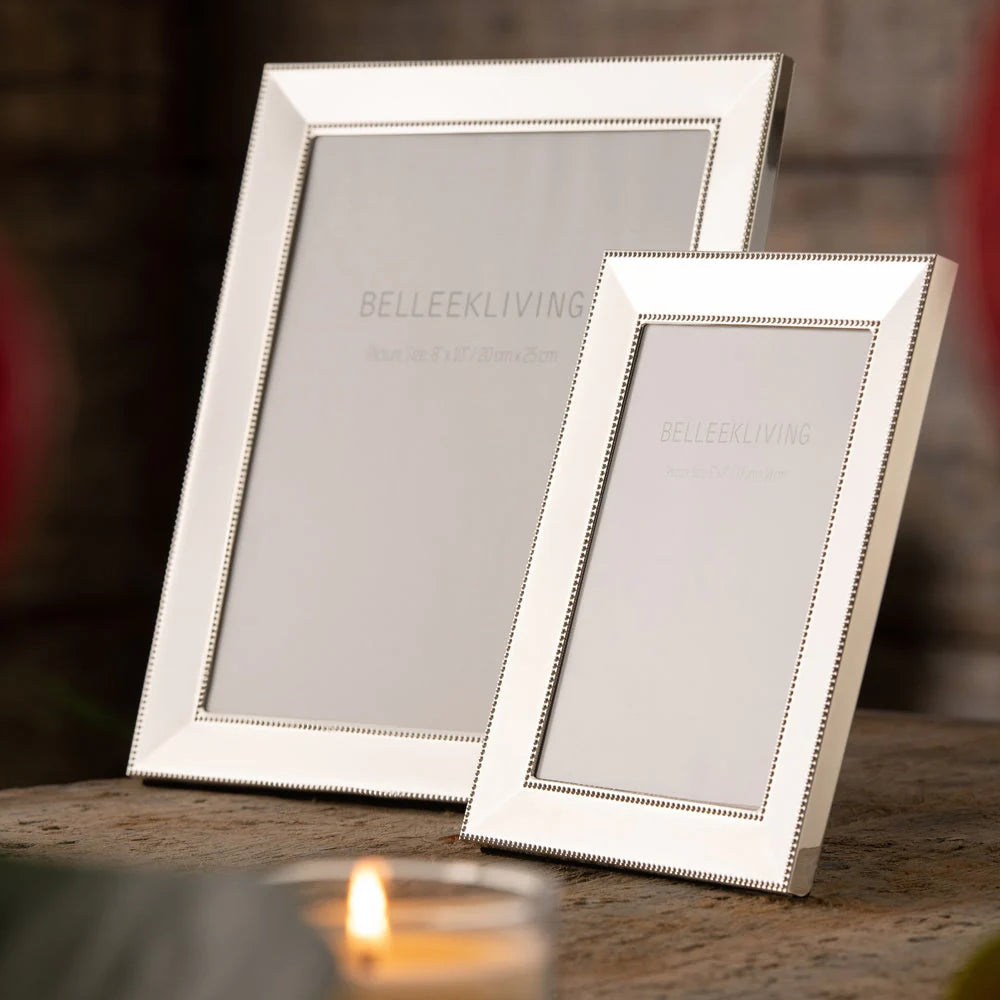 Two polished silver Belleek Living Border photo frames, one 8x10 and one smaller, on a wooden surface.