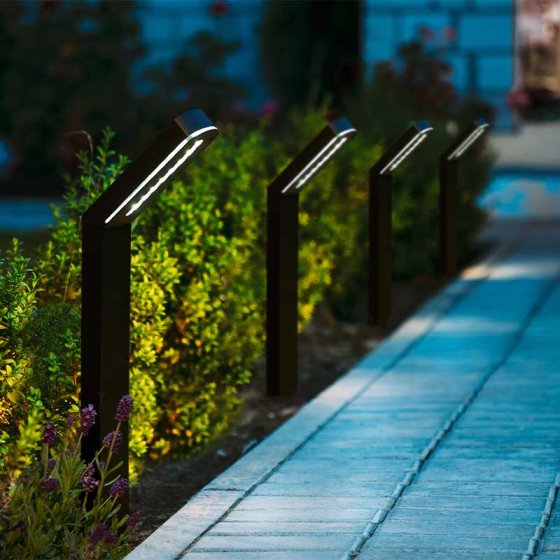 Four Moderna Stake Light 50 Lumen fixtures lighting a garden path with warm white light at dusk.