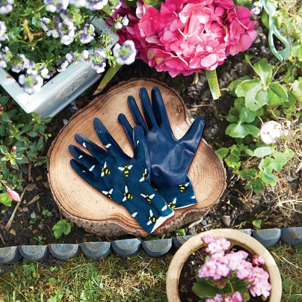 Bees Seed & Weed Gardening Gloves M8 with bee pattern, navy palms, displayed on a tree stump outdoors.