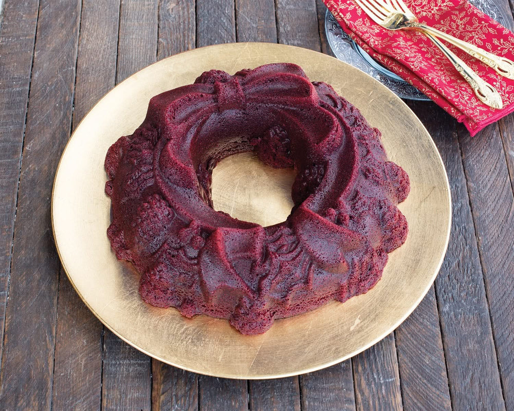 Red velvet cake shaped like a holiday wreath with bow, on a gold plate with red napkin and gold utensils nearby