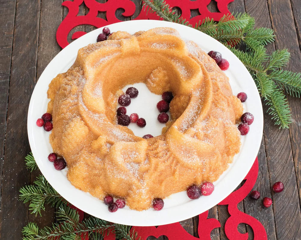Golden bundt cake shaped like a holiday wreath with powdered sugar and cranberries on a white plate