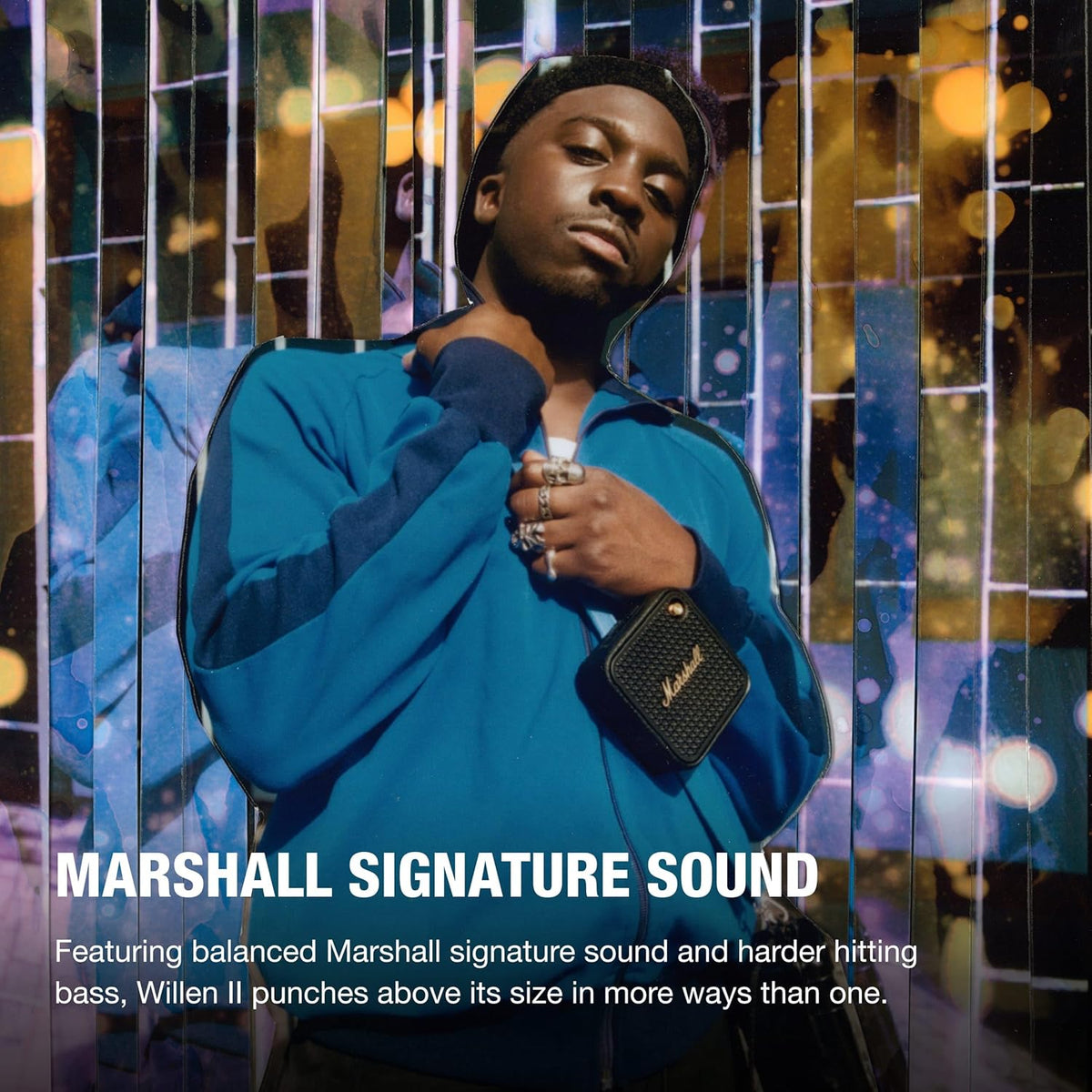 Person wearing a blue jacket holding a Marshall Willen II Black & Brass portable speaker around their neck.